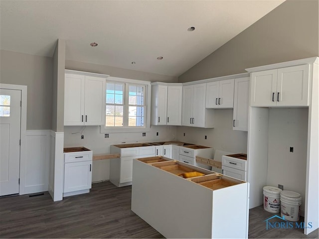 kitchen with a wainscoted wall, dark wood finished floors, a center island, white cabinetry, and vaulted ceiling