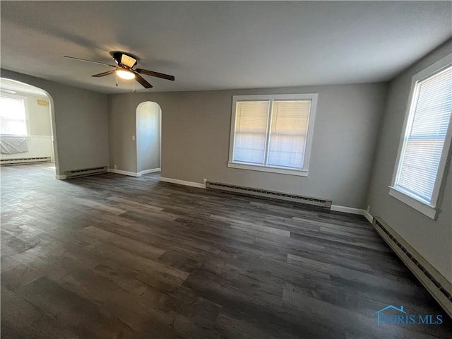 spare room featuring dark wood-style floors, a baseboard radiator, and arched walkways