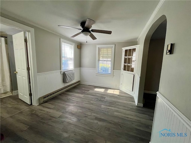 unfurnished room with arched walkways, a baseboard heating unit, wood finished floors, wainscoting, and crown molding