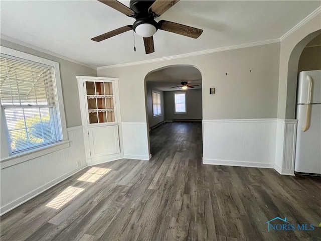 spare room with dark wood-style floors, arched walkways, ornamental molding, a ceiling fan, and wainscoting