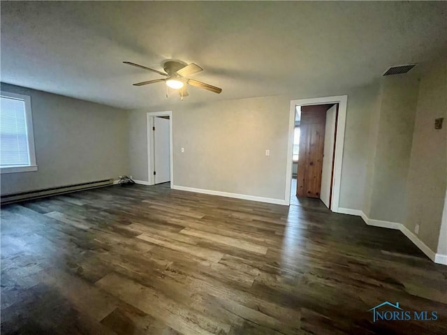 spare room featuring ceiling fan, a baseboard heating unit, visible vents, baseboards, and dark wood finished floors