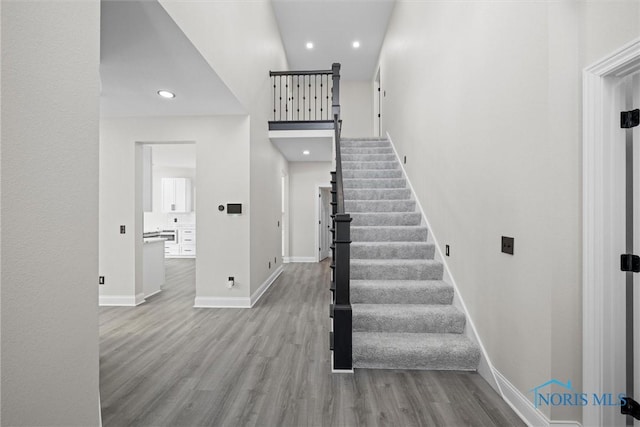 stairs with recessed lighting, a towering ceiling, baseboards, and wood finished floors