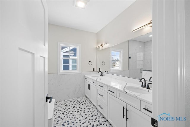 full bathroom with double vanity, a sink, tile walls, and a shower stall