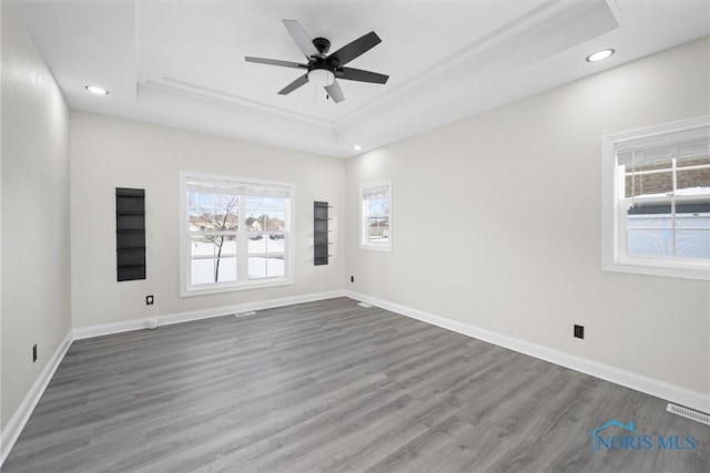 empty room with a raised ceiling, visible vents, dark wood finished floors, and baseboards