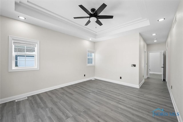 spare room featuring baseboards, visible vents, dark wood-type flooring, a tray ceiling, and recessed lighting