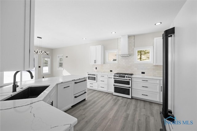 kitchen featuring a sink, white cabinets, double oven range, wall chimney range hood, and decorative backsplash