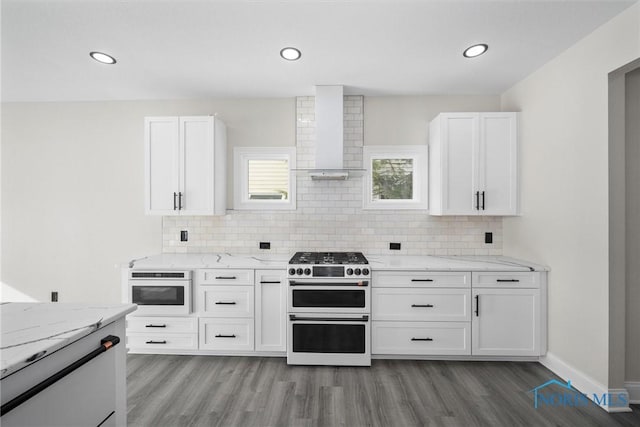 kitchen featuring light stone counters, backsplash, white cabinets, double oven range, and wall chimney exhaust hood