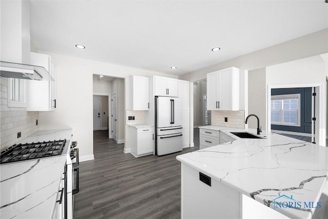 kitchen with a sink, high end white fridge, light stone countertops, wall chimney exhaust hood, and stainless steel range with gas stovetop