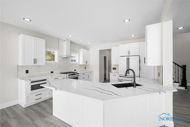 kitchen featuring tasteful backsplash, a sink, wall chimney range hood, white appliances, and a peninsula