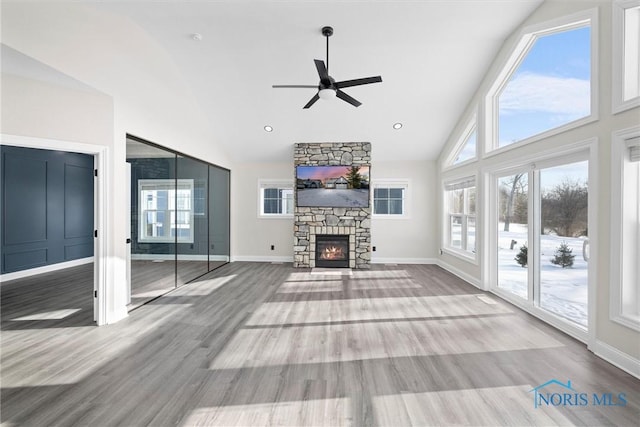 unfurnished living room featuring a ceiling fan, a stone fireplace, baseboards, and wood finished floors