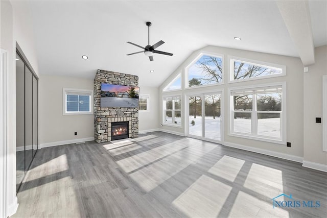 unfurnished living room featuring high vaulted ceiling, a stone fireplace, wood finished floors, and baseboards