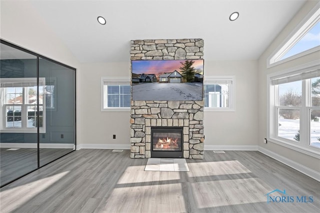 unfurnished living room featuring vaulted ceiling, a stone fireplace, and baseboards