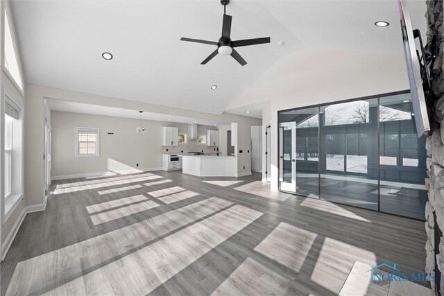 unfurnished living room with ceiling fan, high vaulted ceiling, wood finished floors, and baseboards