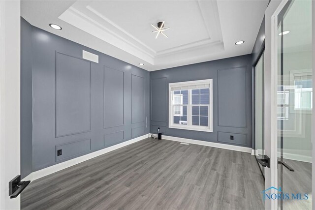 unfurnished room featuring a tray ceiling, a decorative wall, recessed lighting, and wood finished floors