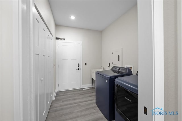 clothes washing area with washing machine and clothes dryer, a sink, light wood-type flooring, laundry area, and baseboards