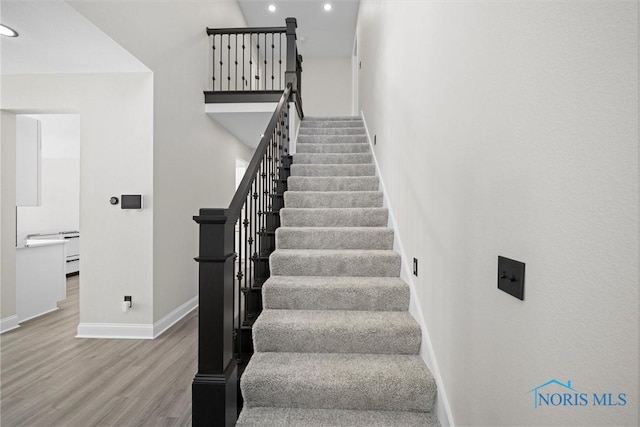 stairs with recessed lighting, wood finished floors, a towering ceiling, and baseboards