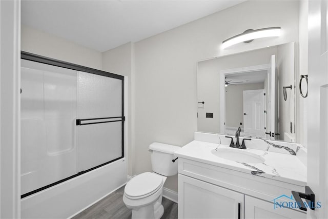 bathroom with baseboards, toilet, enclosed tub / shower combo, wood finished floors, and vanity