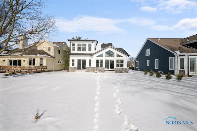 snow covered house featuring stone siding