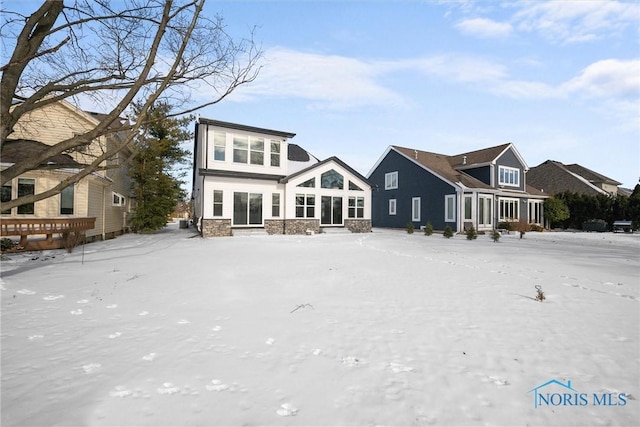 snow covered back of property featuring stone siding