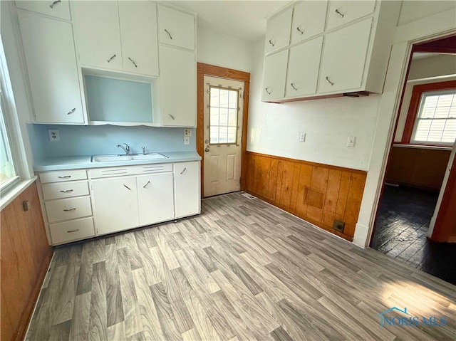 kitchen featuring a sink, white cabinets, light countertops, wainscoting, and light wood finished floors