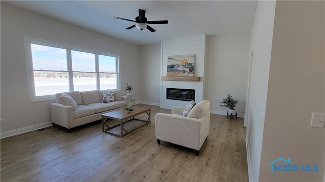 living area with a fireplace, light wood-style flooring, baseboards, and ceiling fan