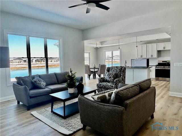 living room with ceiling fan with notable chandelier, light wood-style floors, and baseboards