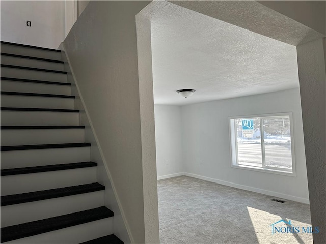 stairs with a textured ceiling, a textured wall, carpet flooring, visible vents, and baseboards