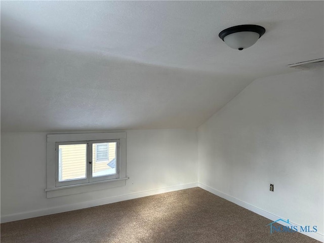 additional living space with baseboards, vaulted ceiling, a textured ceiling, and dark colored carpet