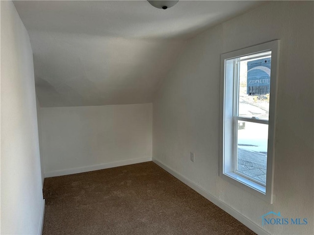 bonus room with dark colored carpet, lofted ceiling, and baseboards