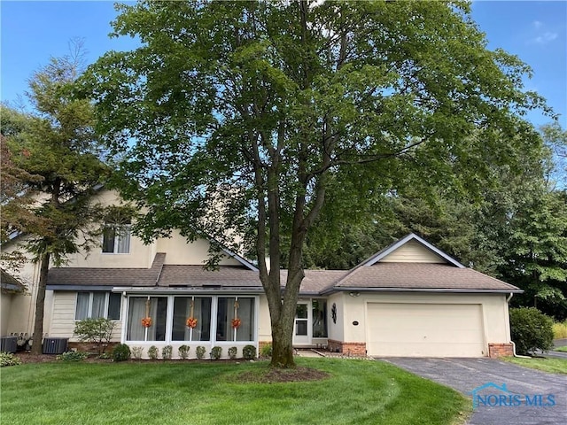 view of front of property featuring central air condition unit, a garage, aphalt driveway, and a front yard