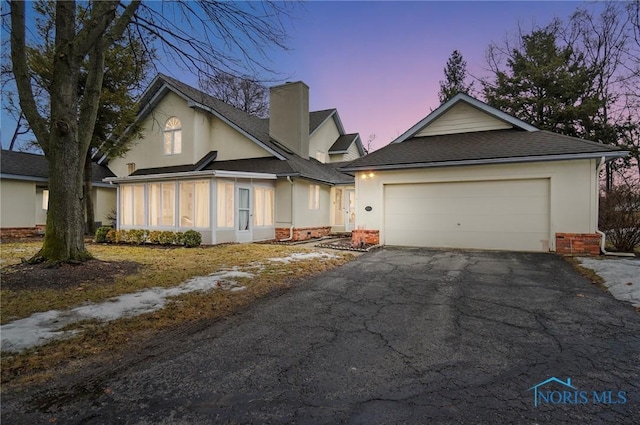 view of front of house featuring aphalt driveway, an attached garage, a shingled roof, stucco siding, and a chimney