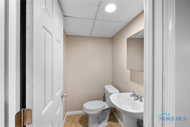 half bath with toilet, a sink, a drop ceiling, baseboards, and tile patterned floors