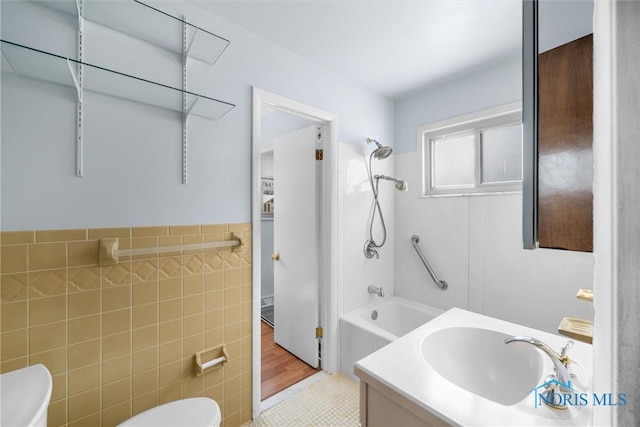 full bathroom with tile walls, toilet, washtub / shower combination, wainscoting, and vanity