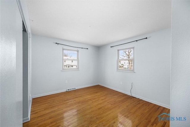 empty room with wood finished floors, visible vents, and baseboards