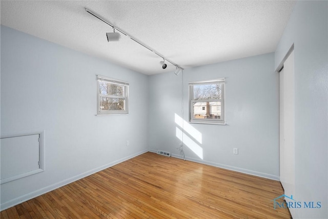 spare room with light wood-style floors, visible vents, baseboards, and a textured ceiling