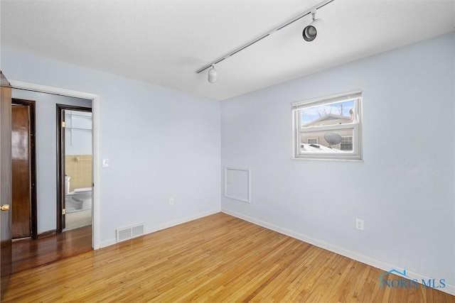 spare room with light wood-type flooring, rail lighting, baseboards, and visible vents