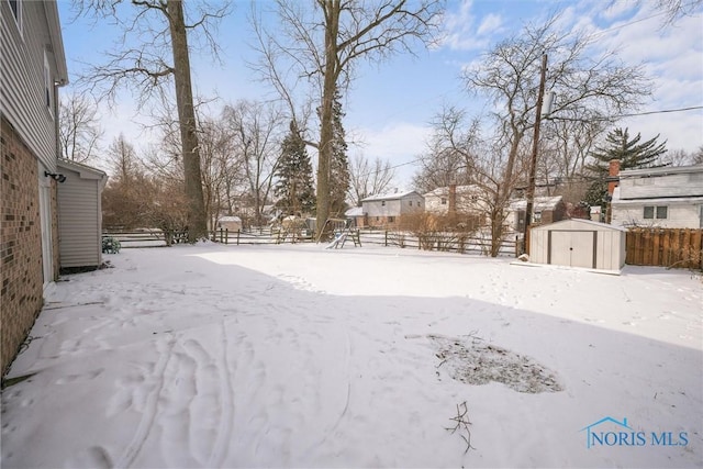 snowy yard with a storage shed, an outbuilding, and fence