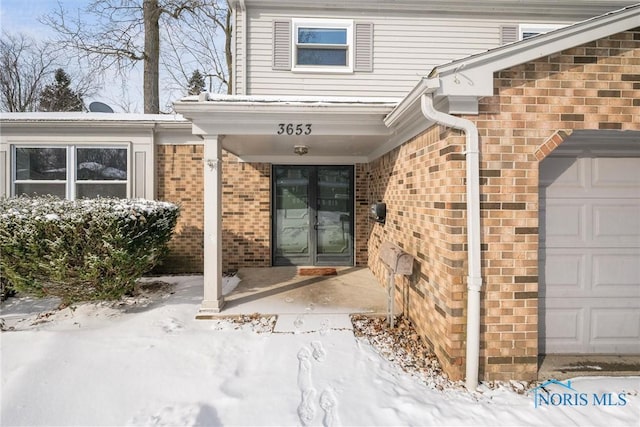 snow covered property entrance with a garage and brick siding