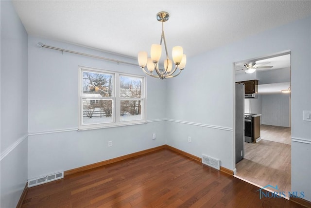 spare room featuring ceiling fan with notable chandelier, dark wood finished floors, visible vents, and baseboards