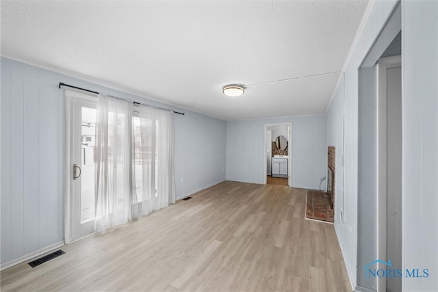 unfurnished living room featuring light wood-style floors, a brick fireplace, visible vents, and crown molding