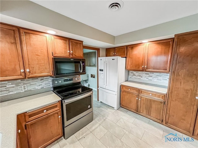 kitchen with white refrigerator with ice dispenser, visible vents, brown cabinetry, stainless steel electric range, and light countertops