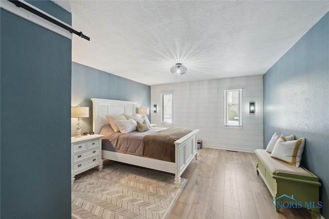 bedroom with a textured wall, light wood-style flooring, a textured ceiling, and a barn door