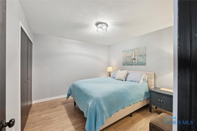 bedroom with light wood-style flooring, a closet, baseboards, and a textured ceiling