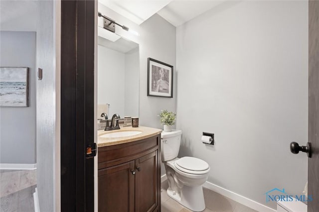 half bath with toilet, tile patterned flooring, baseboards, and vanity