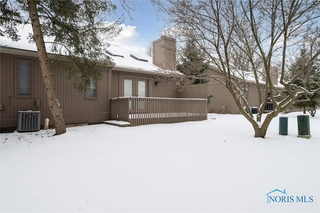 snow covered back of property with a chimney and central AC unit