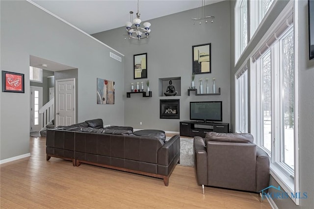 living room featuring light wood finished floors, stairway, a high ceiling, a chandelier, and baseboards