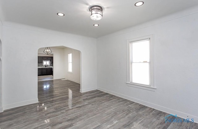 unfurnished room with baseboards, arched walkways, dark wood-type flooring, a sink, and recessed lighting