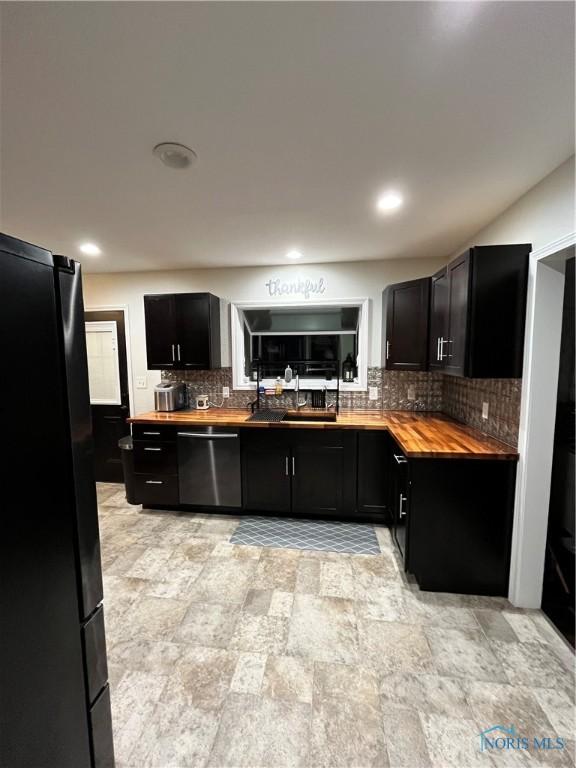 kitchen with backsplash, a sink, wood counters, dark cabinetry, and black appliances