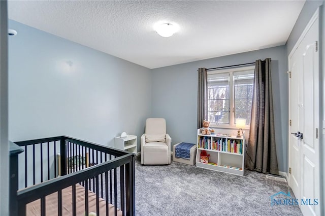 carpeted bedroom with a nursery area, a textured ceiling, and baseboards