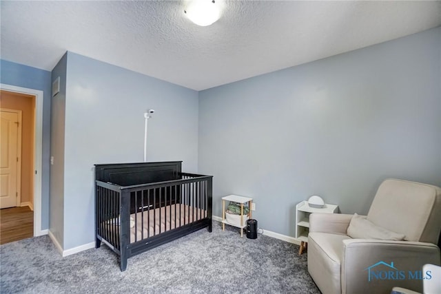 carpeted bedroom with a textured ceiling, a nursery area, and baseboards